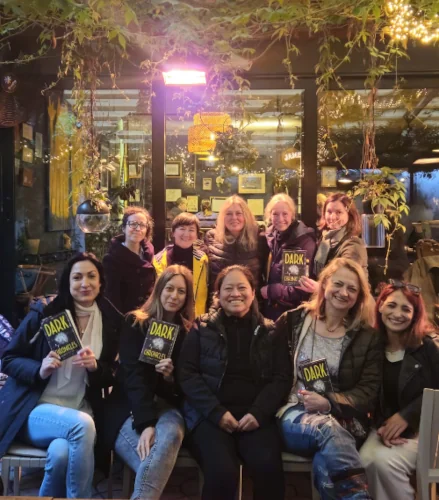 A group of of ten women in front of a restaurant, some are hlding 'Dark Chronicles' paperback copy in their hands